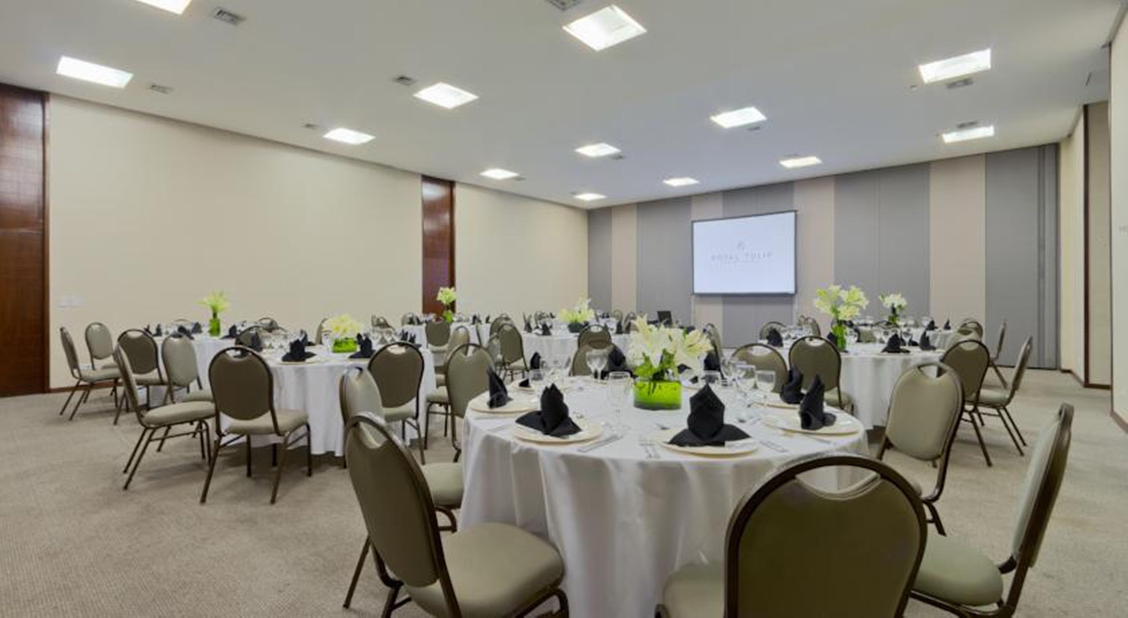 Royal Tulip Brasilia Alvorada Hotel Exterior foto The photo shows a banquet or conference room set up with multiple round tables covered in white tablecloths. Each table is arranged with black napkins and centerpieces featuring flowers, likely in shades of green and white. The room has beige walls a